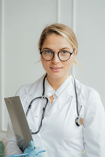 Smiling female healthcare professional in white coat holding clipboard indoors. HD phone wallpaper