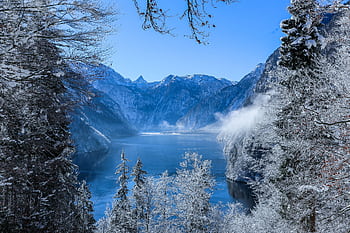 Serene winter landscape of a snowy lake surrounded by mountains and frosty trees. HD wallpaper