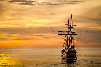 A majestic pirate ship sails into the serene waters at sunset, casting a dramatic silhouette. HD wallpaper