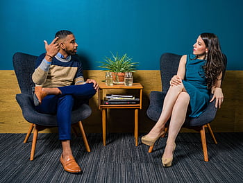Two professionals in business attire engage in a thoughtful discussion sitting in a stylish, modern room. HD wallpaper
