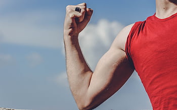 Close-up of a flexed arm in a red shirt against a clear blue sky, symbolizing strength and empowerment. HD wallpaper