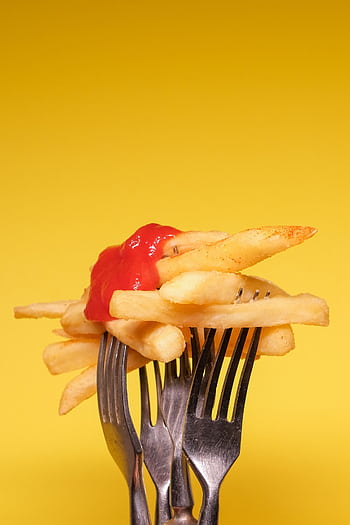 Golden french fries with ketchup on forks against a yellow background. HD phone wallpaper