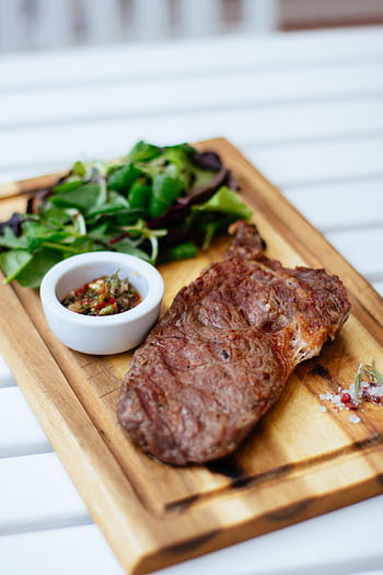 Juicy grilled steak served with fresh herb salad and sauce on a wooden board. HD phone wallpaper