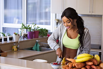 Smiling woman preparing fresh fruit in a sunlit kitchen, embodying a healthy lifestyle. HD wallpaper