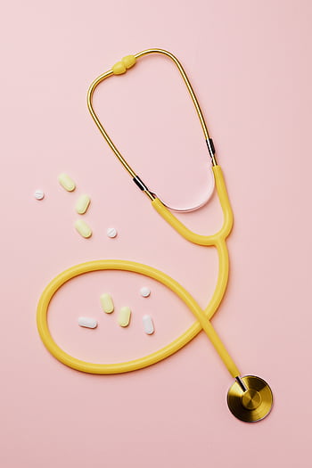 Flat lay of a yellow stethoscope and assorted pills on a pastel pink background. HD phone wallpaper