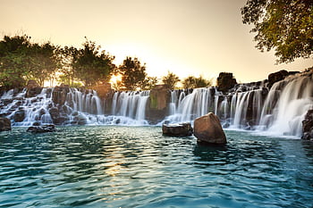 A serene waterfall surrounded by rocks and trees at sunset, radiating tranquility. HD wallpaper