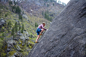 A climber in shorts skillfully ascends a steep rock face in a scenic mountainous environment. HD wallpaper