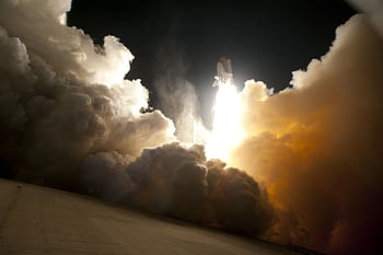 A dramatic of a space shuttle launching into the night sky, surrounded by billowing smoke and intense light. HD wallpaper