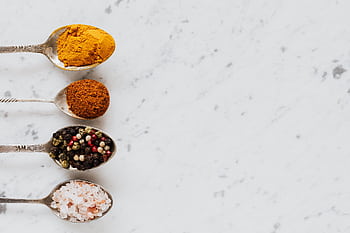An assortment of colorful spices on spoons laid on a marble surface. HD wallpaper