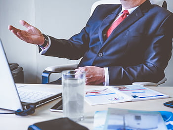 Professional man gesturing in a business meeting at an office desk, conveying confidence and leadership. HD wallpaper