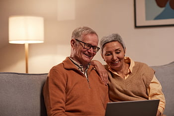 Senior couple enjoying time together on laptop indoors, smiling and relaxed. HD wallpaper