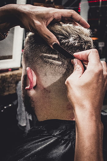 A man receives a detailed haircut with a straight razor at a barbershop, showcasing modern style. HD phone wallpaper
