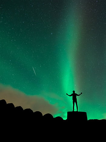 Silhouette of a person admiring the northern lights under a starry sky. HD phone wallpaper