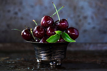 A rustic metal bowl filled with fresh, juicy cherries glistening with moisture. HD wallpaper