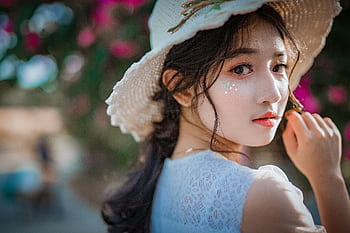 Portrait of a young Asian woman wearing a sun hat, surrounded by vibrant flowers. HD wallpaper