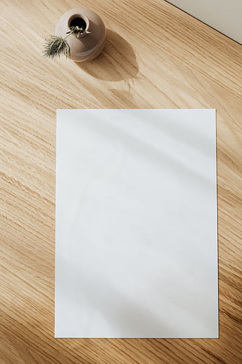 A creative, minimalist desk setup with a blank sheet of paper and a small decorative vase on a wooden surface. HD phone wallpaper