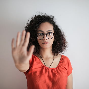 A serious woman with curly hair and glasses making a stop gesture against a white background. HD phone wallpaper