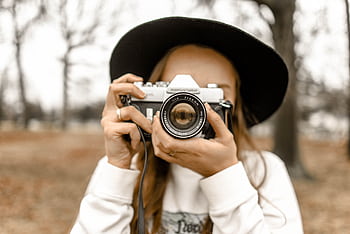 Stylish woman in black hat holding a vintage camera outdoors during fall. HD wallpaper