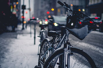 A bicycle covered in snow on a city street with blurred traffic and lights in the background. HD wallpaper