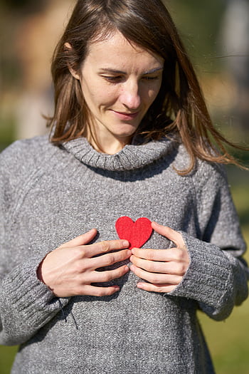 A woman outdoors holding a red heart against her chest, capturing a warm moment. HD phone wallpaper