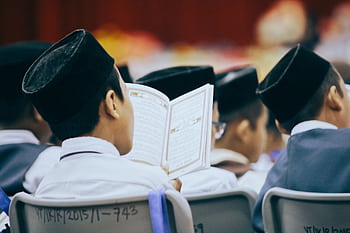 Boys in traditional attire reading the Quran during a religious gathering, showcasing faith and devotion. HD wallpaper