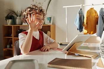 Happy child waving during an online learning session at home. HD wallpaper