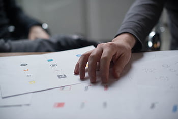 A close-up shot of a hand reviewing various logo designs on paper, ideal for business concepts. HD wallpaper