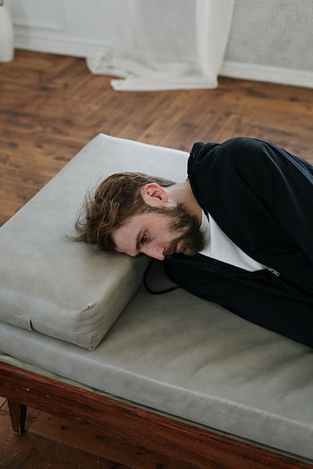 A man lies on a couch indoors, appearing deep in thought or contemplative mood. HD phone wallpaper
