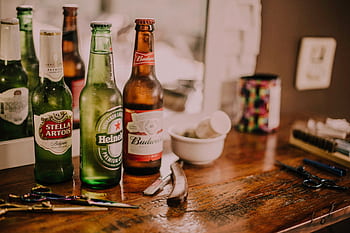 Beer bottles and barber tools on a wooden barbershop counter with a blurred mirror reflection. HD wallpaper