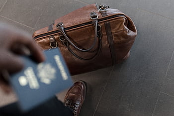 Brown leather bag with passport in an airport setting, ideal for travel and fashion themes. HD wallpaper