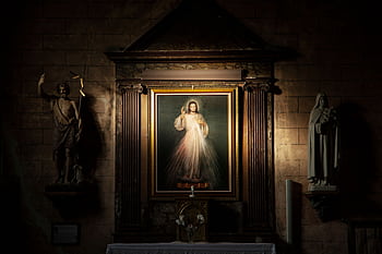 A framed religious portrait flanked by statues inside a dimly lit French church. HD wallpaper