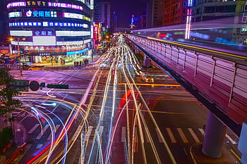Dynamic city intersection with colorful light trails and neon lights at night, showcasing urban motion and energy. HD wallpaper