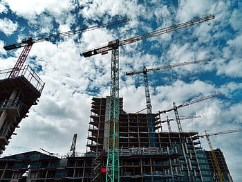 Urban construction site with numerous cranes framing rising skyscrapers against a blue sky. HD wallpaper