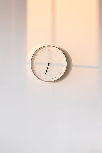 Elegant minimalist wall clock casting warm shadows on a simple backdrop. HD phone wallpaper