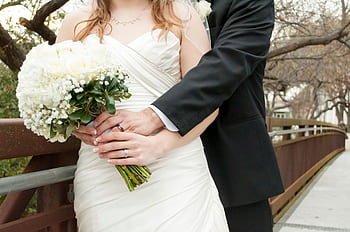 Bride and groom embracing outdoors holding a bouquet, symbolizing romance and love. HD wallpaper