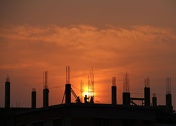 Silhouette of workers on a construction site against a vibrant sunset sky. HD wallpaper