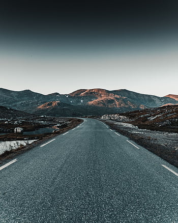 Empty road leading to mountains at twilight with dramatic skies and serene atmosphere. HD phone wallpaper