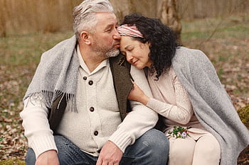 Senior couple enjoying a warm embrace in a serene autumn park, showcasing love and companionship. HD wallpaper