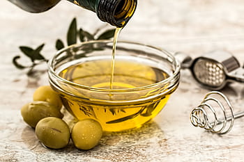 Close-up of olive oil being poured into a glass bowl surrounded by fresh olives and kitchen tools. HD wallpaper
