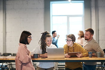 A group of young professionals collaborating indoors with laptops and tablets. HD wallpaper