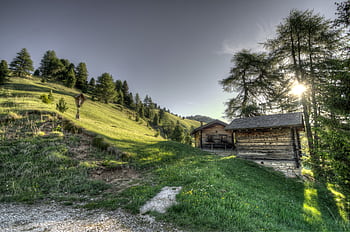 Beautiful countryside landscape with wooden cabins on a hillside during sunset, evoking serenity and nature's tranquility. HD wallpaper