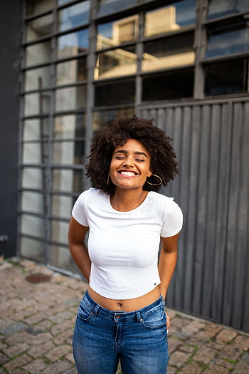 Smiling woman with curly hair in casual fashion enjoys a bright day outdoors. HD phone wallpaper