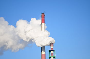 A tall industrial smokestack releasing thick white smoke against a clear blue sky. HD wallpaper