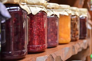 A close-up view of various homemade jam jars lined up on a wooden shelf. HD wallpaper