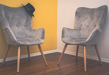 Two contemporary gray armchairs in a minimalist interior with a yellow accent wall and wooden flooring. HD wallpaper
