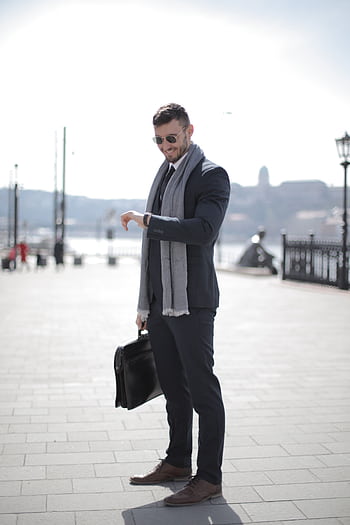 A confident businessman in a suit outdoors checking his watch, holding a briefcase. HD phone wallpaper