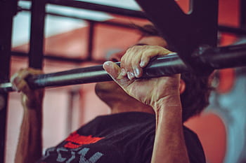 Focused shot of a man doing pull-ups in a gym, highlighting his strength and endurance. HD wallpaper