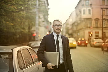 Businessman in a suit holding a laptop on a busy city street. Urban professional life. HD wallpaper
