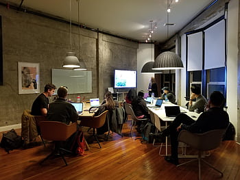 Diverse team collaborating in a modern office setting with laptops and presentation screen. HD wallpaper