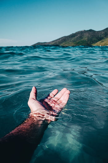 A serene hand emerges from the vibrant ocean waves at Arraial do Cabo under daylight. HD phone wallpaper